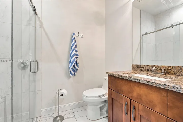 Bathroom featuring a walk-in shower with glass enclosure, stone-finish countertop, wood-finish vanity cabinetry, and large-format tile flooring