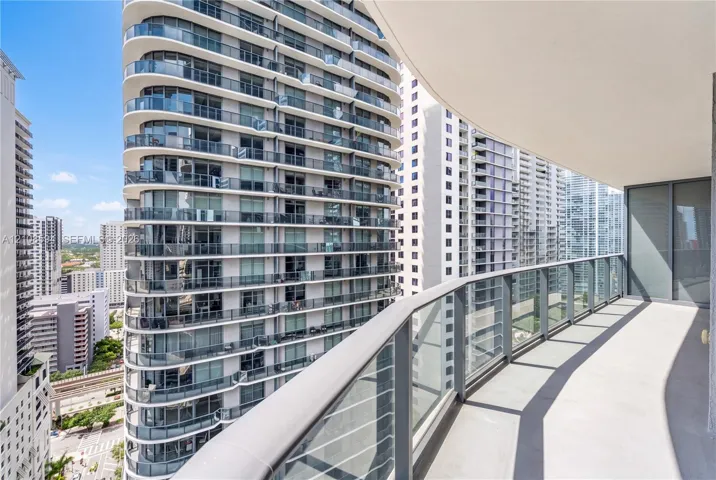 Covered outdoor balcony featuring a curved structural design, concrete flooring, and metal railing with glass panels