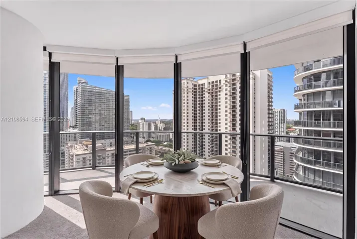 Curved floor-to-ceiling windows, wrap-around private balcony with metal railing, and neutral wall-to-wall carpeting