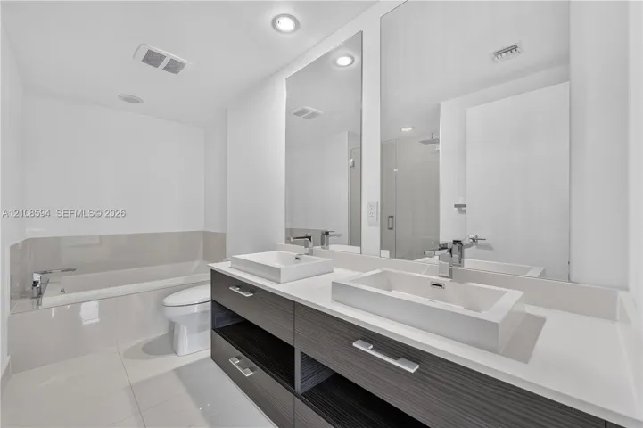 Modern floating vanity featuring dual rectangular vessel sinks, a solid surface countertop, wood-finish cabinetry, and polished chrome fixtures, complemented by floor-to-ceiling mirrors and a deep soaking tub