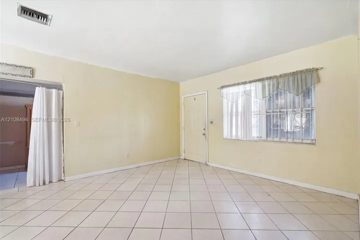 Interior space featuring diagonal-patterned ceramic tile flooring, neutral wall paint, and a window equipped with metal security bars