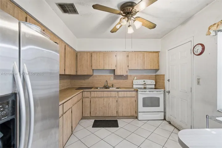 Kitchen featuring wood-finish cabinetry, stainless steel refrigerator, white free-standing range, double-basin sink, and tile flooring