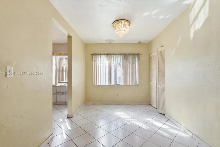 Neutral tile flooring, built-in louvered closet doors, and decorative crystal-style flush mount ceiling lighting