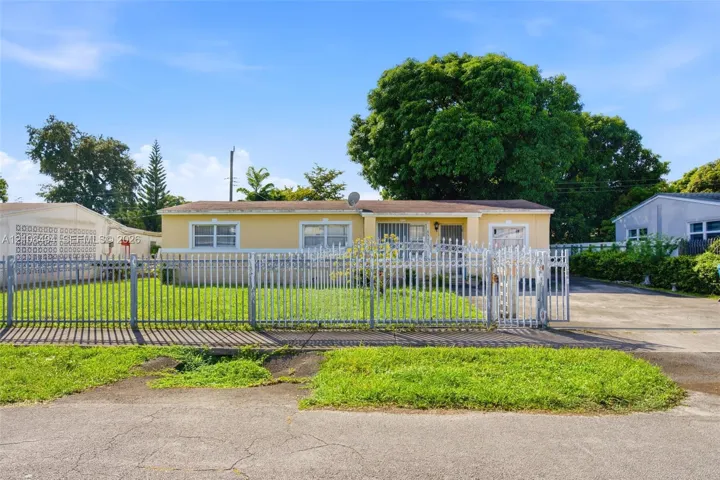 Single-story residence featuring a stucco exterior, concrete driveway, metal picket fencing, and mature trees
