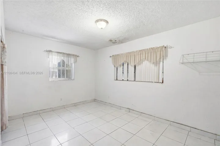 Interior space featuring white floor tiles, a dual-window configuration, a flush-mount ceiling light fixture, and a built-in wire wall shelf