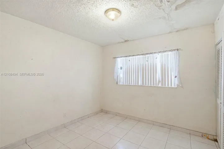 Room featuring white tile flooring, ceiling-mounted flush lighting, and a louvered bi-fold closet door