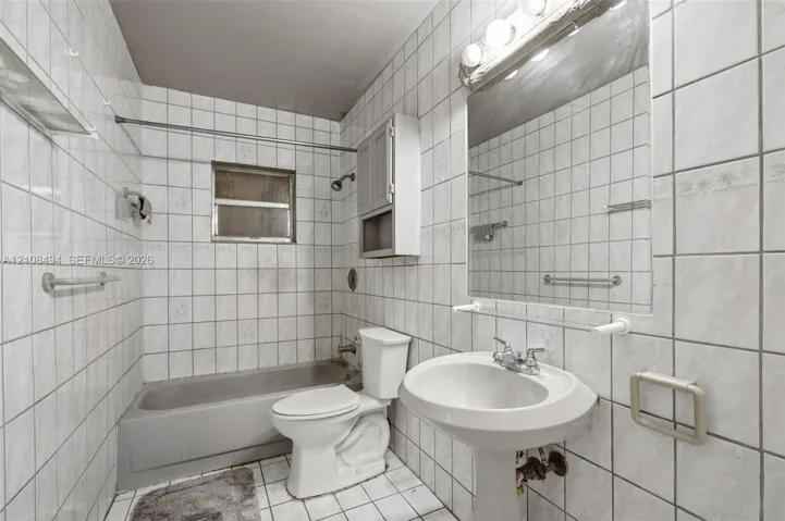 Full-height tile wall surround, white pedestal sink, integrated wall-mounted medicine cabinet, wall-to-wall mirror with glass shelving, and porcelain tub with shower head fixture