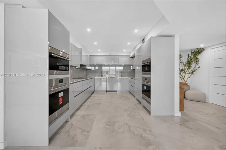 Contemporary kitchen featuring high-gloss cabinetry, built-in stainless steel double ovens, integrated appliances, and large-format tile flooring with recessed lighting