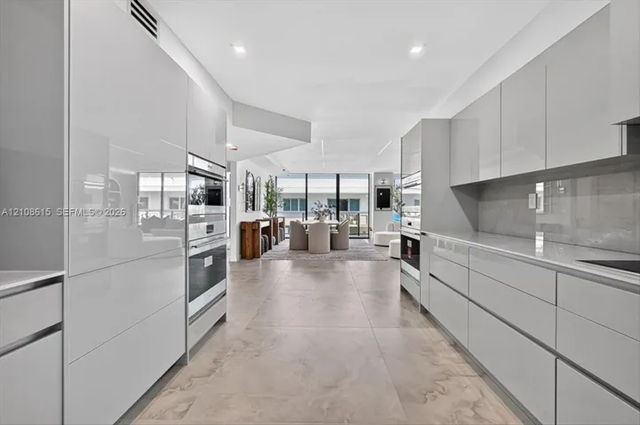 Contemporary kitchen featuring high-gloss cabinetry, large-format tile flooring, stone-surfaced countertops, and built-in stainless steel double ovens