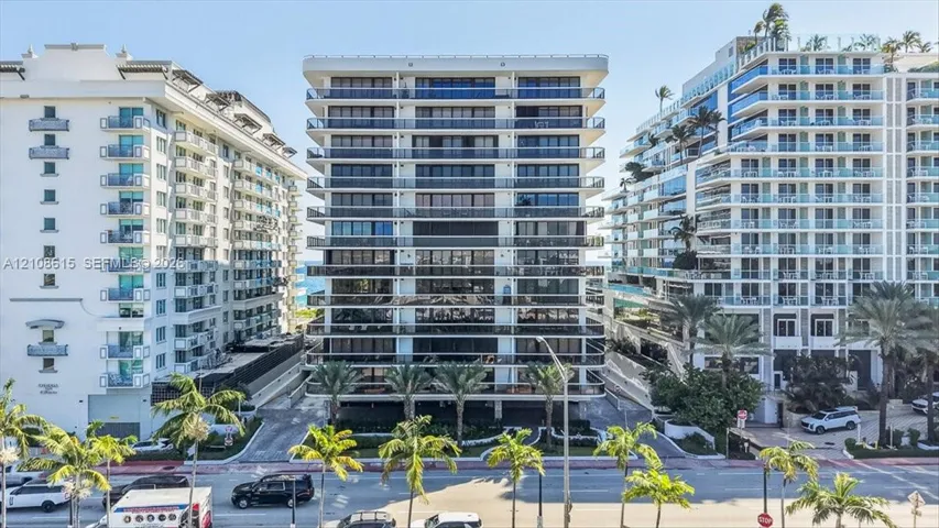High-rise building exterior featuring tiered concrete balconies with glass railings, floor-to-ceiling windows, and mature palm trees