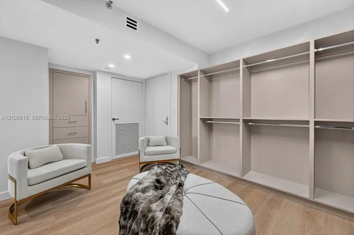 Custom built-in storage system featuring light wood-finish shelving and hanging rods, integrated drawer unit with brushed metal hardware, and wood-finish flooring