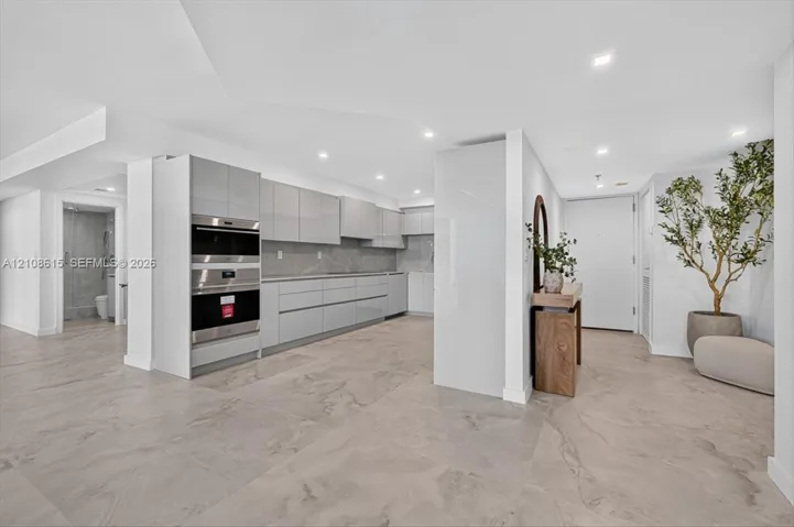 Modern kitchen featuring high-gloss cabinetry, stone-surface countertops, built-in double ovens, and large-format tile flooring with recessed lighting