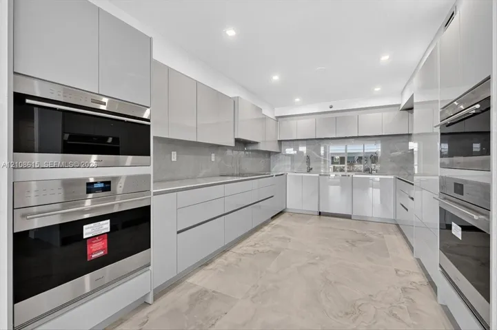 Modern kitchen featuring high-gloss cabinetry, stone-finish tile flooring, integrated stainless steel ovens, and recessed lighting