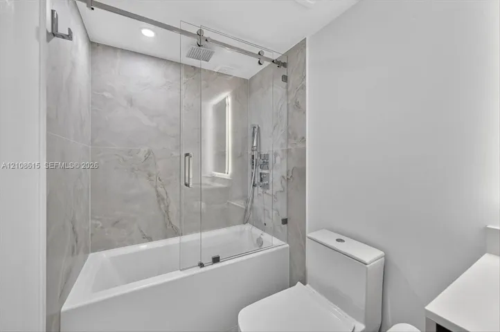 Shower with glass sliding enclosure, floor-to-ceiling stone-finish tile surround, ceiling-mounted rainfall showerhead, and integrated handheld fixture