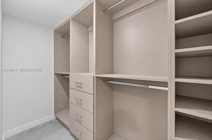 Custom reach-in closet featuring light-toned cabinetry, four integrated storage drawers, chrome hardware, multiple shelving tiers, and brushed metal hanging rods