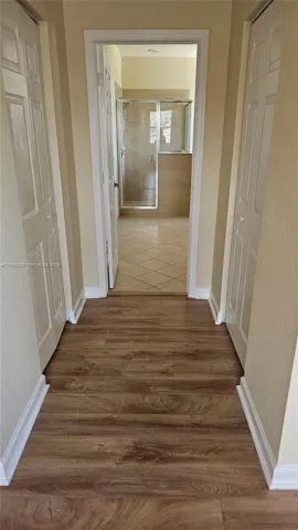 Wood-finish flooring, two sets of paneled closet doors, and tiled flooring leading to a glass-enclosed shower