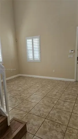 High-ceiling interior featuring tiled flooring, plantation shutters, and a wood-finish staircase railing