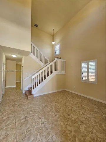 Two-story foyer featuring volume ceilings, tile flooring, a staircase with white balusters, and windows with interior plantation shutters