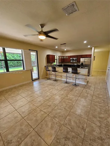 Kitchen featuring dark wood cabinetry, a stone-accented breakfast bar, stainless steel appliances, large-format tile flooring, and a ceiling fan