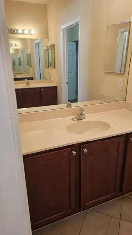 Vanity featuring dark wood cabinetry, an integrated basin, a neutral-toned countertop, a multi-bulb light fixture, and a large-format mirror