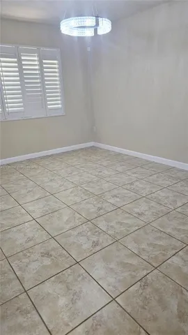 Neutral-toned tile flooring, circular tiered chandelier, and multi-panel window with plantation shutters