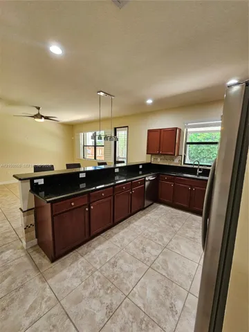 Kitchen featuring dark-toned cabinetry, stone-finish countertops, tile flooring, stainless steel dishwasher, and a multi-light pendant fixture over the breakfast bar
