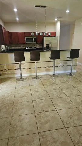 Kitchen featuring a peninsula island, stainless steel appliances, tile flooring, stone-tiled backsplash, and overhead pendant lighting