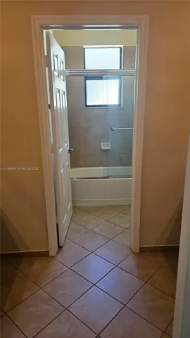 Bathroom featuring tile flooring, a shower-tub combination with stone-finish wall tile, a glass sliding enclosure, and a rectangular window