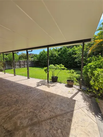 Covered patio with stamped concrete flooring, grass lawn, and perimeter wood fencing