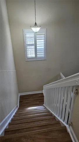 Staircase featuring wood-finish treads, a white balustrade, a window with interior shutters, and a pendant light fixture