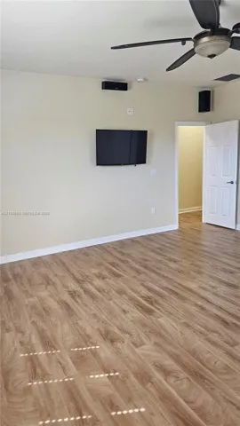 Wood-finish flooring, ceiling fan with integrated lighting, wall-mounted display hardware, and a paneled interior door
