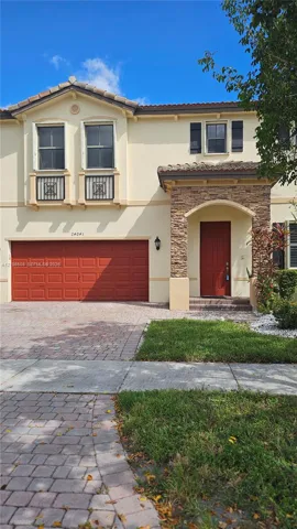 Two-story exterior featuring stucco siding, decorative stone masonry at the entryway, a paver driveway, arched entryway, and metal Juliet balcony railings