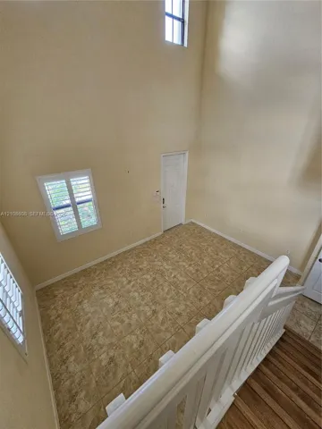 Double-height ceiling featuring tall vertical windows, tile flooring, and a white wood-finish staircase railing