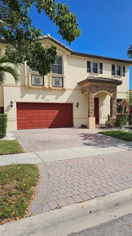 Stucco exterior with stone veneer accents at the arched entryway, decorative metal balcony railings, a multi-car garage, and a paver driveway
