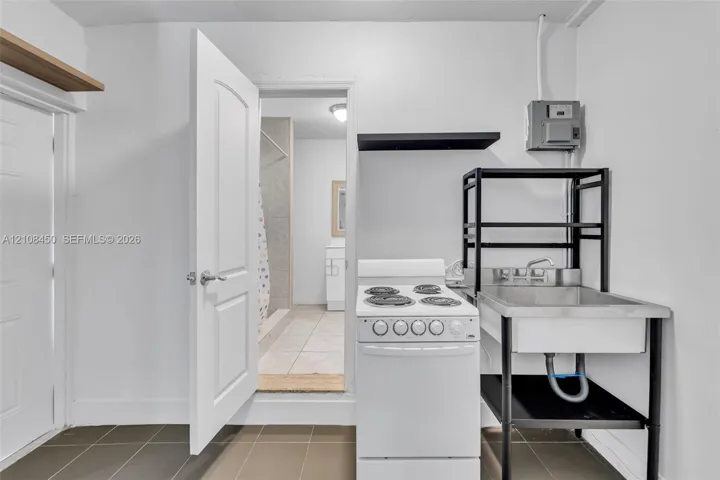 Utility space featuring dark-tone tile flooring, a white electric range, and a stainless steel basin with a metal frame