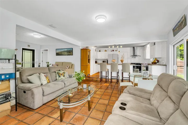 Open-concept interior featuring terracotta tile flooring, white cabinetry, a kitchen island, and sliding glass patio doors
