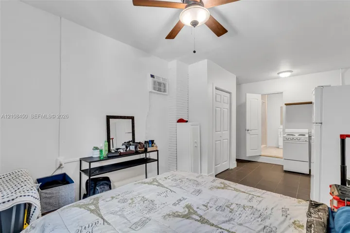 Room featuring white walls, a ceiling fan with integrated lighting, dark tile flooring, a wall-mounted cooling unit, and a built-in pantry