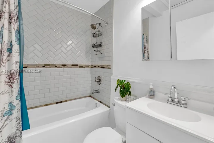 Full bathroom featuring a tub-shower combination with herringbone and subway tile surround, integrated vanity with an oval basin, and a mirrored medicine cabinet
