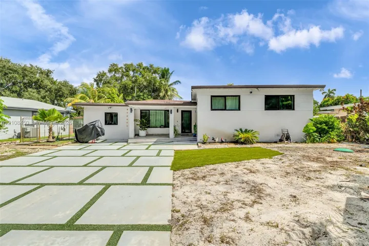 Single-story exterior featuring a white smooth-finish facade, large-format concrete paver driveway with turf inlays, and dark-framed windows