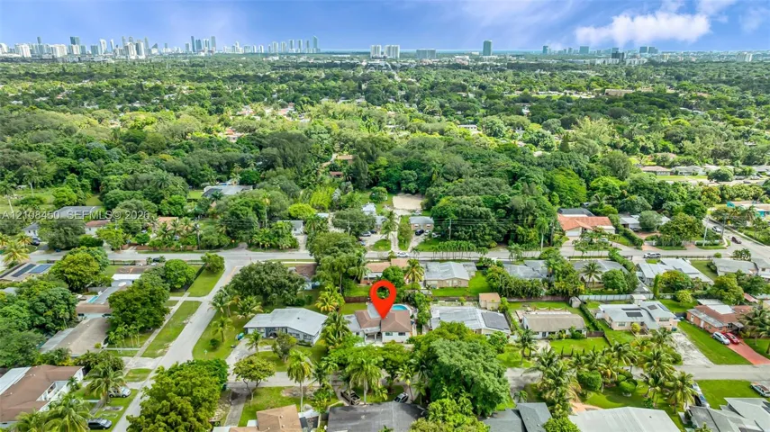 Aerial perspective featuring a property with a swimming pool, situated within a landscape of mature trees and established residential vegetation, incorporating a backdrop of an urban skyline