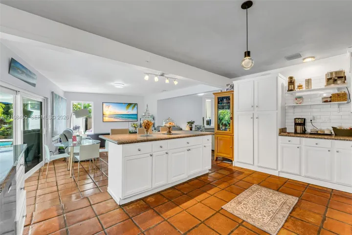 Kitchen featuring a central island with a stone countertop, white shaker-style cabinetry, white subway tile backsplash, and terracotta tile flooring