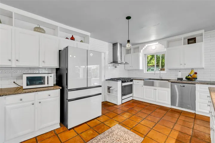 Kitchen featuring white shaker cabinetry, stainless steel apron-front sink, stone-finish countertops, ceramic tile flooring, and subway tile backsplash