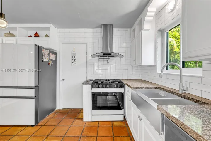 Kitchen featuring white shaker cabinetry, herringbone-patterned subway tile backsplash, stainless steel farmhouse sink, granite countertops, and terra-cotta tile flooring