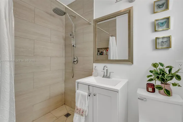 Bathroom featuring large-format neutral wall tile, rain-style showerhead, white vanity cabinet with a rectangular basin, and a framed mirror