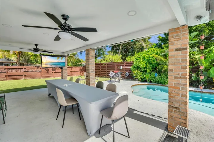 Covered patio featuring a concrete floor, brick support columns, dual ceiling fans, and recessed lighting, overlooking a swimming pool and fenced backyard