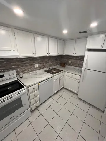 Kitchen featuring white cabinetry, stone-patterned countertops, a decorative tile backsplash, recessed lighting, and tile flooring