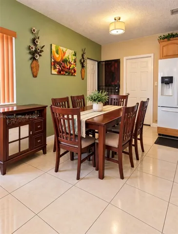 Dining area featuring polished light-toned floor tiles, a drum-style ceiling light fixture, wood cabinetry, and vertical blind window treatments