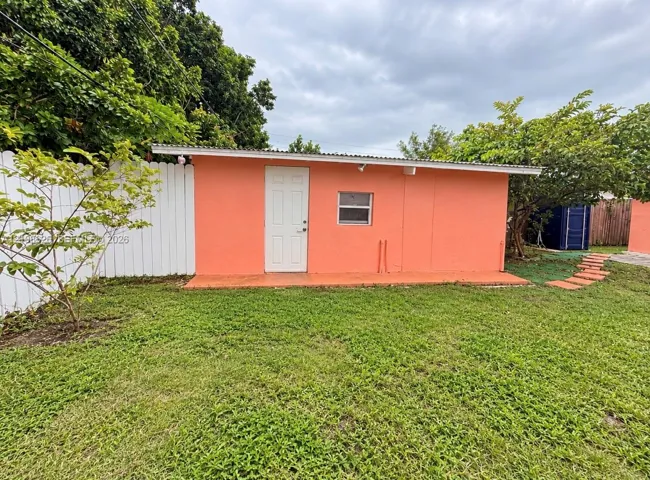 Detached structure featuring a stucco exterior, single-entry door, corrugated metal roofing, and a white privacy fence