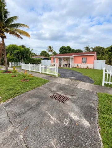 Single-story exterior featuring a vibrant stucco finish, stone-veneer foundation, covered front porch with columns, white picket fencing, and paved driveway