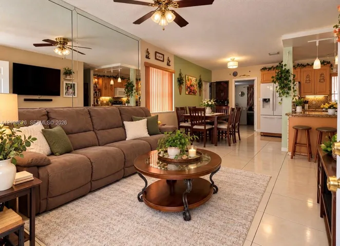 Open-concept living and dining area featuring large-format tile flooring, mirrored wall accent, breakfast bar with pendant lighting, and built-in wooden cabinetry
